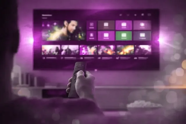 A viewer pointing a remote at a television menu of channels and films