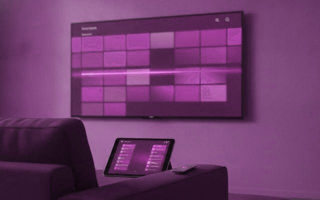 A TV showing a programme guide grid with a tablet and phone showing channel lists on a sofa