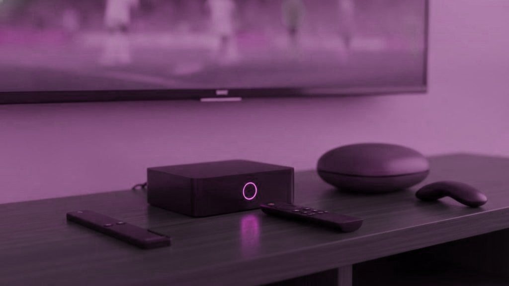 A streaming stick, a set-top box and a round streaming box with their remotes on a TV console
