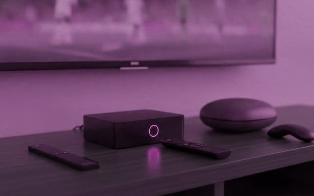 A streaming stick, a set-top box and a round streaming box with their remotes on a TV console