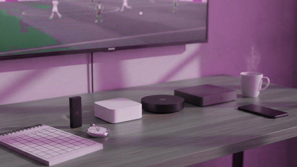 Five streaming devices, a notebook scoring grid and a stopwatch in front of a TV showing a football match